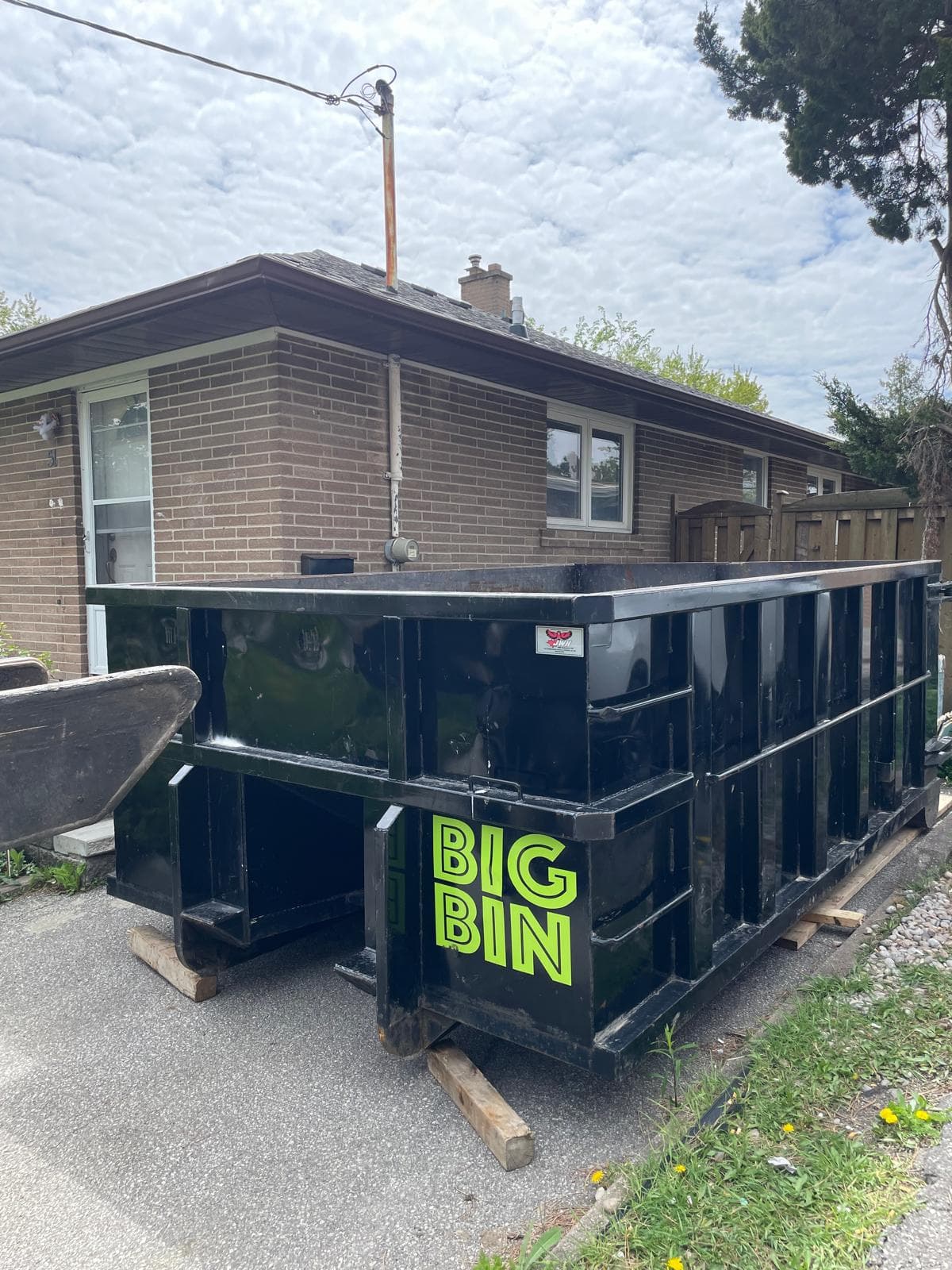 Big Bin roll-off bin resting on wooden protection planks on a residential driveway