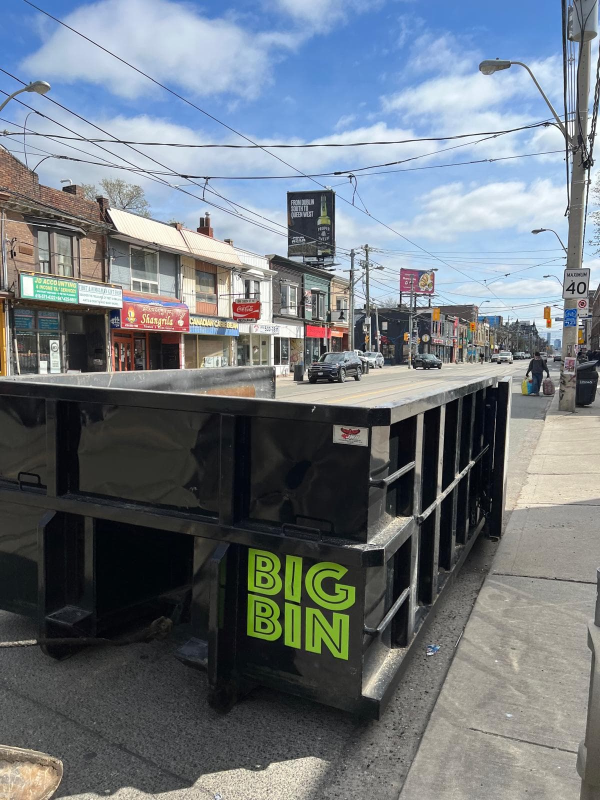 A Big Bin roll-off bin on the sidewalk of Queen Street West in Toronto, streetcar wires overhead
