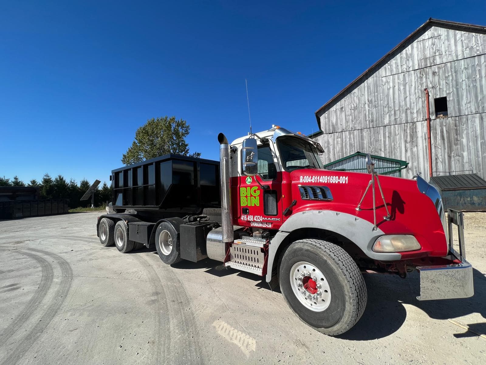 A red Big Bin roll-off truck carrying a black bin against a clear blue sky