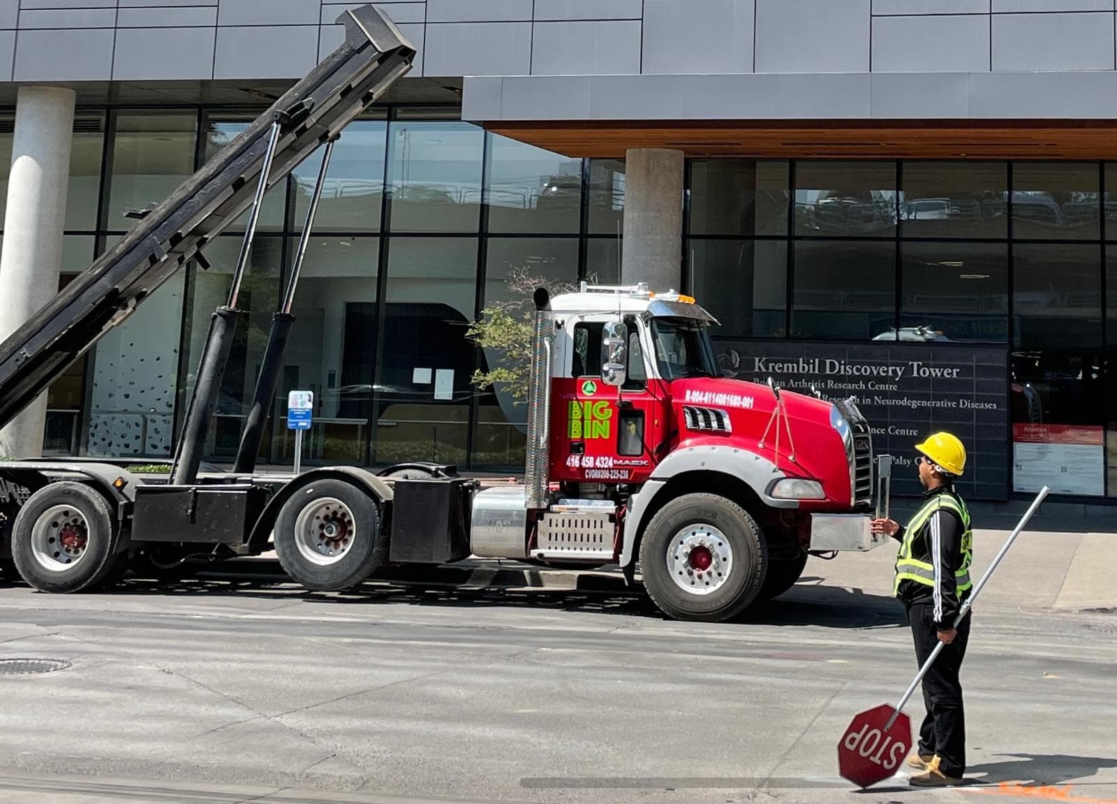 A Big Bin truck working outside a downtown Toronto institution, with a worker in high-visibility gear holding a stop paddle